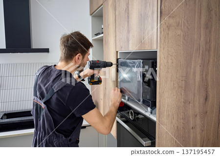 Technician Fixing Microwave Oven in Kitchen Cabinet Technician Fixing Microwave Oven in Kitchen Cabinet 137195457
