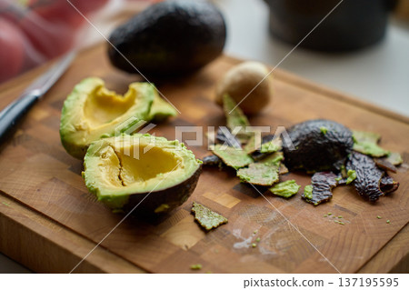 Avocado halves with pit and peel scraps on wooden cutting board 137195595