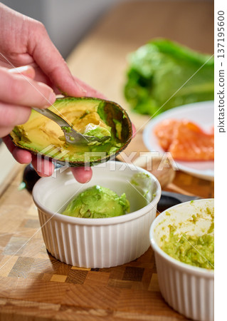 Hands scooping avocado into ramekin on wooden cutting board close up Hands scooping avocado into ramekin on wooden cutting board close up 137195600