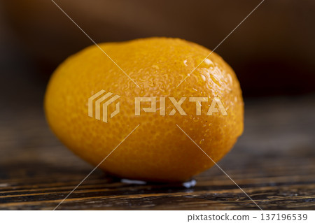 wet small orange fruits of juicy and fragrant kumquat on a black wooden table, oval oblong kumquat fruit covered with drops of water and scattered on a black table made of pine wood wet small orange fruits of juicy and fragrant kumquat on a black wooden table, oval oblong kumquat fruit covered with drops of water and scattered on a black table made of pine wood 137196539