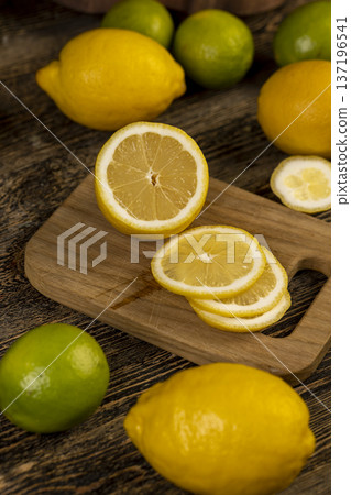 sliced juicy sour lemon lying on the table with green limes, sliced ripe citrus fruits lemon and limes are lying on a wooden table sliced juicy sour lemon lying on the table with green limes, sliced ripe citrus fruits lemon and limes are lying on a wooden table 137196541