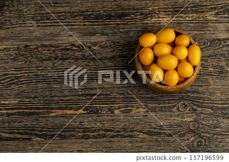 small orange fruits of juicy fresh and fragrant kumquat on a black wooden table, oval oblong kumquat fruit scattered on a black table made of wood 137196599