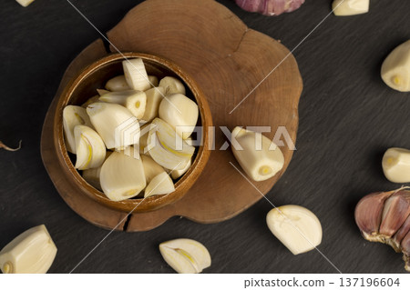 peeled purple garlic scattered on the black kitchen table and peeled and sliced fragrant fresh and natural garlic spices scattered on the kitchen table during cooking peeled purple garlic scattered on the black kitchen table and peeled and sliced fragrant fresh and natural garlic spices scattered on the kitchen table during cooking 137196604
