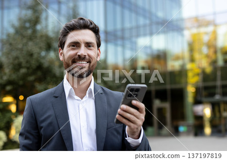 Executive man networking and communicating using a mobile phone, representing remote work, smart technology, and corporate communication in a professional outdoor setting 137197819