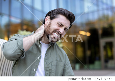 Adult man experiencing acute neck pain, holding his aching neck and shoulder with a pained expression, showing muscle tension and discomfort from stress or long working hours Adult man experiencing acute neck pain, holding his aching neck and shoulder with a pained expression, showing muscle tension and discomfort from stress or long working hours 137197838