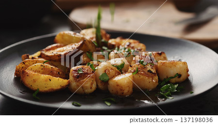 herbs fall over baked potato wedges and roasted scallops on black plate herbs fall over baked potato wedges and roasted scallops on black plate 137198036