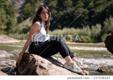 Relaxed Young Woman Resting on Rocks by a Mountain River Relaxed Young Woman Resting on Rocks by a Mountain River 137198267