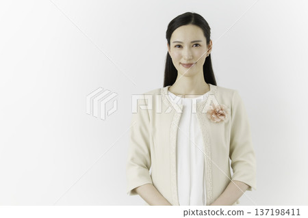 一位年輕的日本女子身穿白色襯衫和米色外套，站在白色背景前，胸前戴著一束鮮花，面帶微笑。 137198411