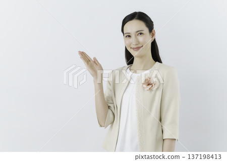 Wearing a white blouse and cream jacket against a white background, she has a flower corsage on her chest and is holding her hand up Wearing a white blouse and cream jacket against a white background, she has a flower corsage on her chest and is holding her hand up 137198413
