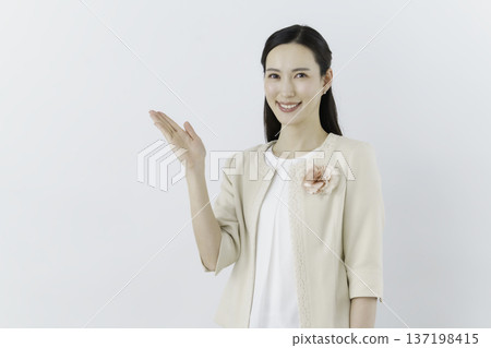 一位身穿白色襯衫和米色外套的女子，站在白色背景前，胸前佩戴著一束花，並用手遮住胸前。 137198415