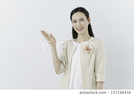 一位身穿白色襯衫和米色外套的女子，站在白色背景前，胸前佩戴著一束花，並用手遮住胸前。 137198416