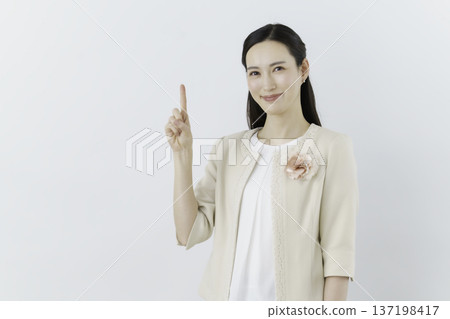 一位身穿白色襯衫和米色外套的女士，站在白色背景上，胸前佩戴著一朵花，擺出數字1的姿勢。 137198417