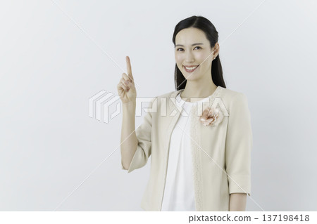 A woman wearing a white blouse and cream jacket on a white background, with a flower corsage on her chest, and posing in the number 1 position 137198418