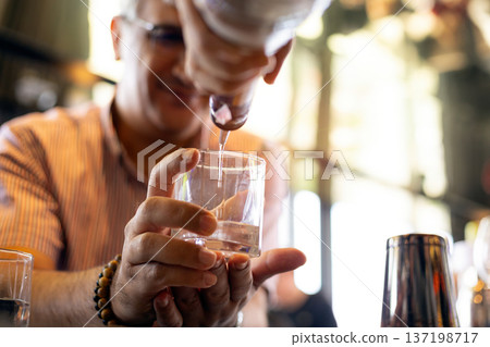 Close up of bartender pouring whiskey into a glass at a stylish bar during a corporate networking event, highlighting executive lifestyle, business celebration and professional social Close up of bartender pouring whiskey into a glass at a stylish bar during a corporate networking event, highlighting executive lifestyle, business celebration and professional social 137198717