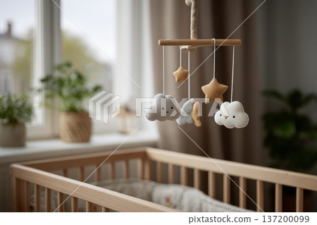 crib mobile gently still above empty crib, soft neutral interior, diffused daylight, calm melancholic atmosphere, horizontal framing 137200099