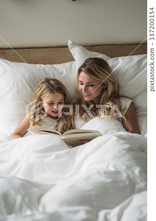mother and daughter reading book together on bed, soft white linens, calm afternoon light, intimate bonding scene, minimalistic bedroom design, vertical orientation 137200154