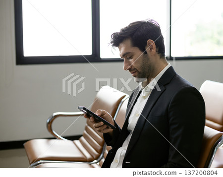 Businessman using smartphone while sitting in waiting area, checking messages and online information, professional mobile communication concept, modern corporate lifestyle Businessman using smartphone while sitting in waiting area, checking messages and online information, professional mobile communication concept, modern corporate lifestyle 137200804