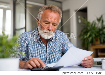 older man reviewing financial documents at desk with calculator, worried facial expression, bright office interior, neutral tones, clean composition, natural daylight 137201585