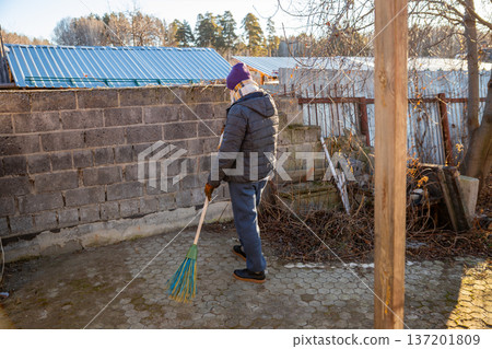 Man sweeping paved yard with broom. Cleaning outdoor area. Manual labor and maintenance at home. Housekeeping chore. Man sweeping paved yard with broom. Cleaning outdoor area. Manual labor and maintenance at home. Housekeeping chore. 137201809
