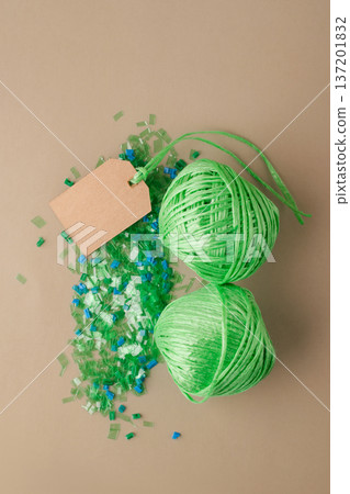 Recycled plastic pellets and skeins of green polyester thread with blank paper tag symbolizing circular sustainability, eco-friendly manufacturing Recycled plastic pellets and skeins of green polyester thread with blank paper tag symbolizing circular sustainability, eco-friendly manufacturing 137201832