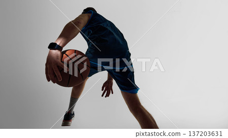Basketball player dribbling ball wearing smartwatch from low angle in studio 137203631