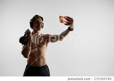 Man taking workout selfie with kettlebell and smartwatch in studio 137203749