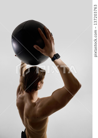 Man holding medicine ball overhead wearing smartwatch in studio. Man holding medicine ball overhead wearing smartwatch in studio. 137203763