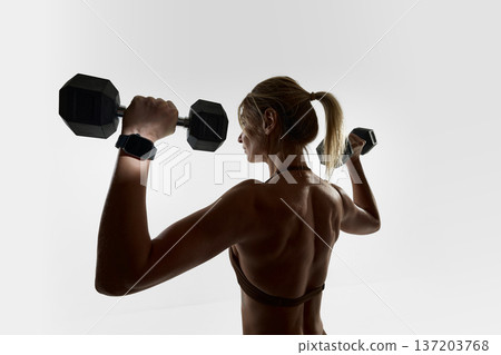 Back view of woman lifting dumbbells wearing smartwatch in studio 137203768