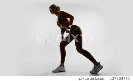 Woman performing bent over dumbbell row wearing smartwatch in studio 137203773