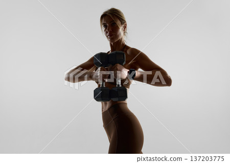 Woman performing dumbbell front raise wearing smartwatch 137203775