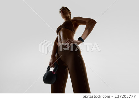 Woman holding kettlebell wearing smartwatch in minimal studio 137203777