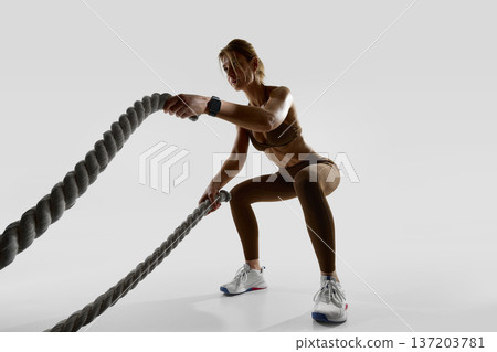 Woman performing battle rope exercise wearing smartwatch in studio Woman performing battle rope exercise wearing smartwatch in studio 137203781