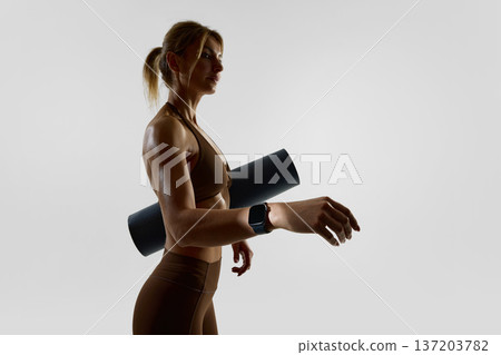 Woman carrying yoga mat wearing smartwatch after workout in studio. Woman carrying yoga mat wearing smartwatch after workout in studio. 137203782