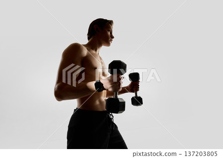 Man training with dumbbells wearing smartwatch in studio. Man training with dumbbells wearing smartwatch in studio. 137203805