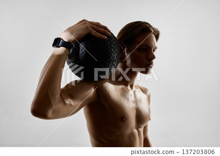 Muscular man holding medicine ball on shoulder wearing smartwatch in studio Muscular man holding medicine ball on shoulder wearing smartwatch in studio 137203806
