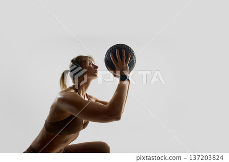 Focused woman holding medicine ball during squat in studio. 137203824