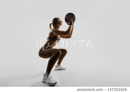 Strong woman squatting with medicine ball and smartwatch. 137203826