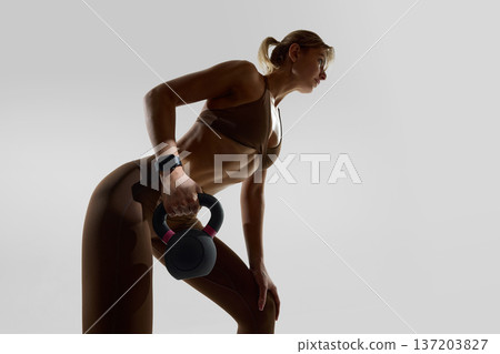Fit woman performing kettlebell row with smartwatch in studio. 137203827