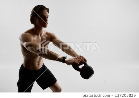 Muscular man training with kettlebell and smartwatch in studio. Muscular man training with kettlebell and smartwatch in studio. 137203829