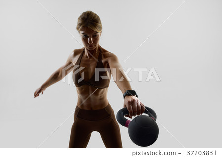 Strong woman performing kettlebell swing with fitness tracker. 137203831