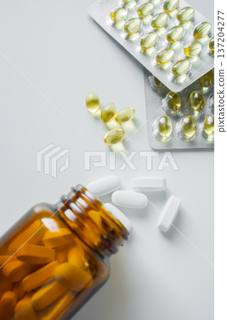 Omega 3 fish oil capsules in blisters and white pills in brown glass bottle on white table close up. Vitamins and supplements, healthcare and medicine Omega 3 fish oil capsules in blisters and white pills in brown glass bottle on white table close up. Vitamins and supplements, healthcare and medicine 137204277