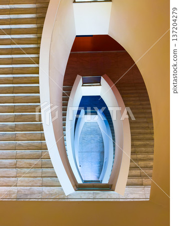 Symmetrical modern spiral staircase viewed from above with curved rails and marble steps Symmetrical modern spiral staircase viewed from above with curved rails and marble steps 137204279