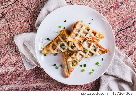 Close up of waffle toasts with ham, cheese and tomato filling on a plate on the table top view Close up of waffle toasts with ham, cheese and tomato filling on a plate on the table top view 137204305