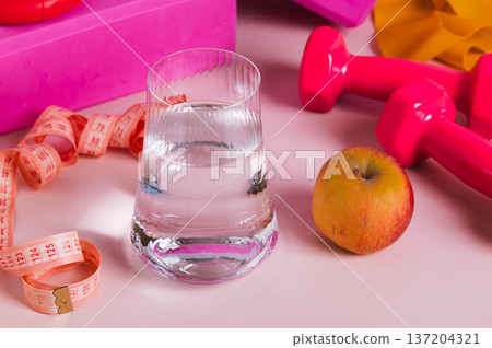 A glass of water and an apple for a diet and sports equipment on the table 137204321