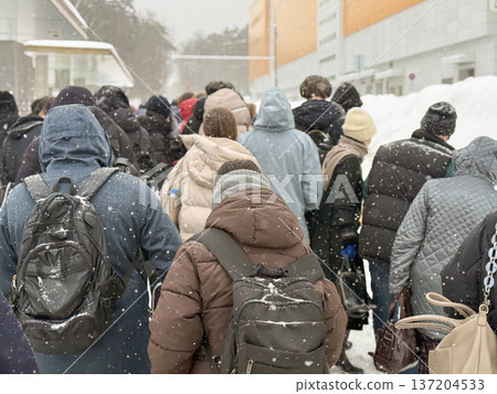 Winter crowd anonymous diverse people standing in queue outdoors, long line of men and women, rear view, snowfall, city district. Public transport, workforce commute, snow season, urban life Winter crowd anonymous diverse people standing in queue outdoors, long line of men and women, rear view, snowfall, city district. Public transport, workforce commute, snow season, urban life 137204533