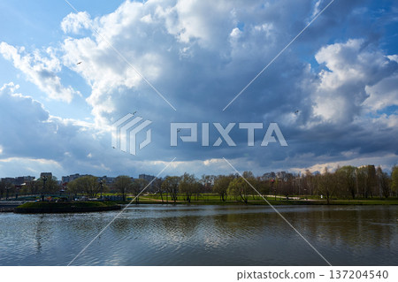 Landscape of urban park with lake and large clouds in blue sky. Nature background. Relaxing view for tranquil scenes Landscape of urban park with lake and large clouds in blue sky. Nature background. Relaxing view for tranquil scenes 137204540