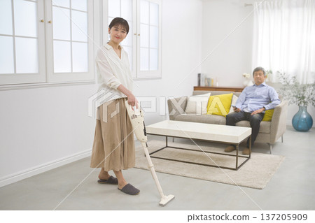A smiling woman and a man in their 60s vacuuming while having a conversation A smiling woman and a man in their 60s vacuuming while having a conversation 137205909