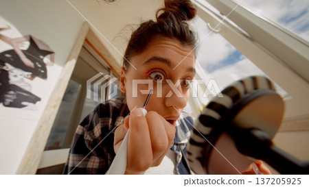 Woman carefully experiments with eyelash tools in natural light 137205925