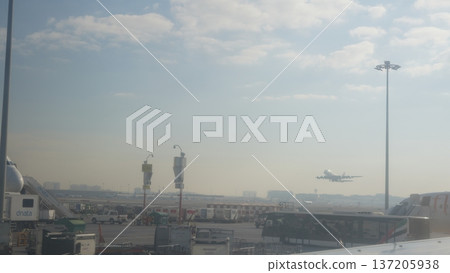 Airplane landing at airport with terminal and ground vehicles visible 137205938