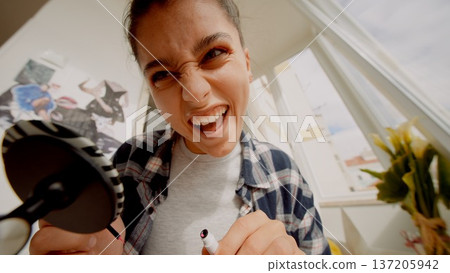 Energetic female smiling and putting on mascara by sunny window 137205942